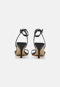 Sandales à talons hauts noires avec lanières, en cuir texturé, avec des lanières étroites autour de la cheville et un petit talon carré.