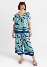 Completo a due pezzi composto da una maglietta a V e pantaloni a gamba larga, entrambi con pattern di foglie verdi e blu con strisce orizzontali. Tessuto leggero.