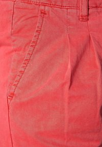 Bomullsblandning byxor i korall med en slät yta, utrustade med sidofickor och subtila plisseringar för extra designdetaljer.