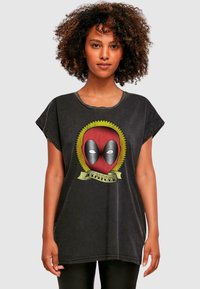 Čierne oversized tričko s vintage štýlovou grafikou červenej masky Deadpoola s žltým slnkom a zeleným bannerom s nápisom "Deadpool."