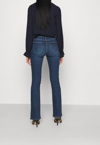 Mörkblå, högmidjade jeans med utsvängda ben, med bakfickor och subtila sömmar. Bärs med en långärmad topp och klackar.