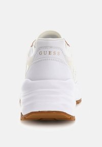 Scarpe da ginnastica bianche con una finitura liscia, dotate di tallone imbottito, suola in gomma e logo "GUESS" in oro impresso sul retro.