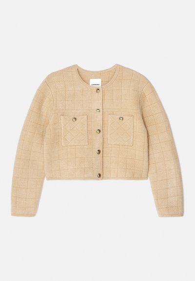 Μπεζ πλισέ καζάκα με στρογγυλή λαιμόκοψη, χρυσό κούμπωμα και δύο τσέπες στο στήθος. Μαλακή υφή με κομμένο μήκος.