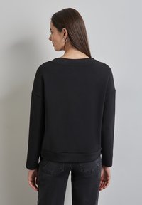Felpa nera con una vestibilità rilassata, scollo rotondo e maniche lunghe. Tessuto liscio, abbinata a jeans scuri, presenta un design minimal.