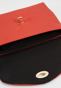 Clutch in pelle sintetica rossa con chiusura dorata, dotata di un interno nero e foderatura rossa lungo i bordi, progettata per un aspetto elegante.