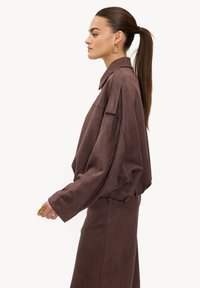 Veste marron oversize avec un col cranté, en tissu doux. Le design comprend des manches larges et une coupe décontractée, associée à un pantalon assorti.