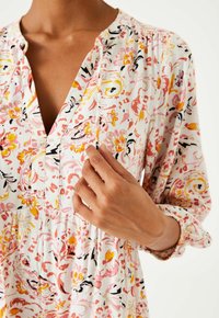 Kwiatowa sukienka z lekkiego materiału, z różowymi, żółtymi i czarnymi wzorami. Dekolt w kształcie litery V z plisowaniem i detalami z guzikami z przodu.