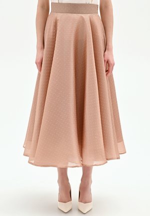 Donna che indossa una gonna midi a vita alta, a trapezio, color marrone chiaro con piccoli pois bianchi e tacchi beige con punta appuntita.