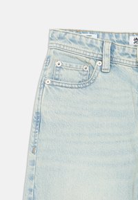 Světlé modré džíny z denimu s vysokým pasem, s výraznou texturou, dvěma předními kapsami, kovovými nýty a viditelným vyblednutím.