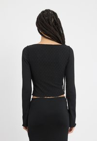 Black long-sleeve cropped top with a textured pattern and straight hem, paired with a fitted black skirt. Seam details are visible.