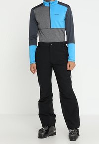 Pantalons de ski noirs associés à un haut à manches longues avec un bloc de couleurs en gris et bleu. Le haut présente un col montant et une fermeture éclair à l'avant.