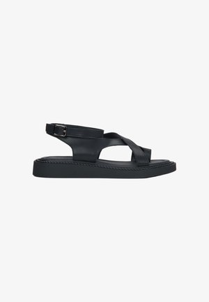Black leather sandal with crossed straps, ankle buckle, and thick textured sole, shown in side profile on a white background.