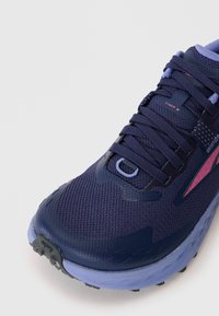 Gros plan sur une chaussure de course bleu marine et violette avec un dessus en maille texturée, des lacets et une semelle en caoutchouc robuste.
