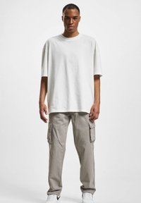 White oversized t-shirt made of cotton, paired with light gray cargo pants featuring side pockets and a relaxed fit; white sneakers.