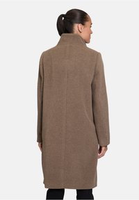Cappotto di lana marrone con collo alto, maniche lunghe e silhouette dritta. Il tessuto appare morbido con una texture liscia e minimalismo nei dettagli.