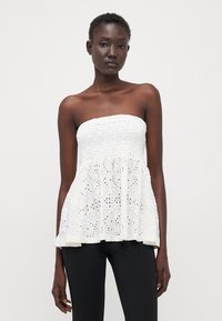 Fehér, pánt nélküli peplum top, smocked melltartó résszel és virágmintás csipkével. Könnyű anyag, texturált részletekkel. Fekete nadrággal párosítva.