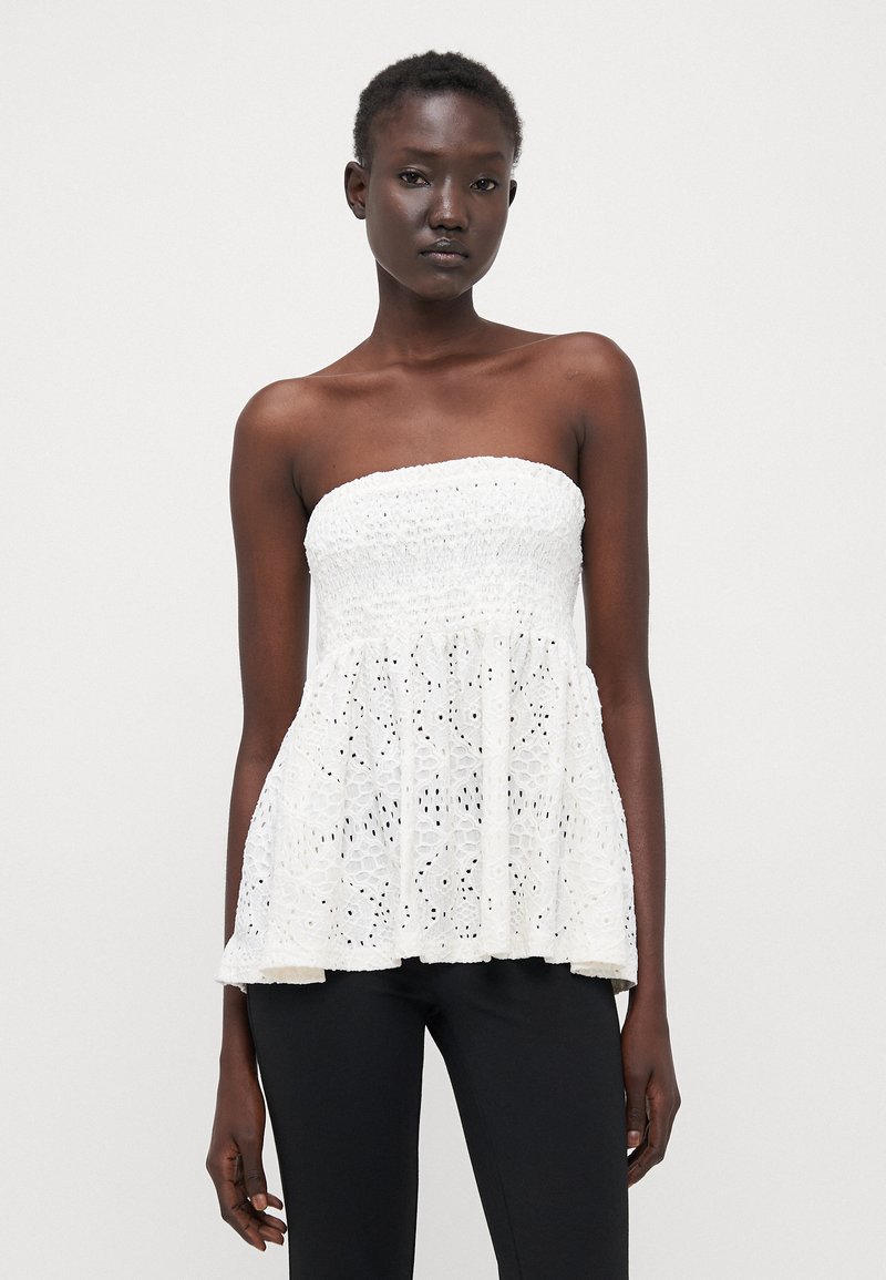 Fehér, pánt nélküli peplum top, smocked melltartó résszel és virágmintás csipkével. Könnyű anyag, texturált részletekkel. Fekete nadrággal párosítva.