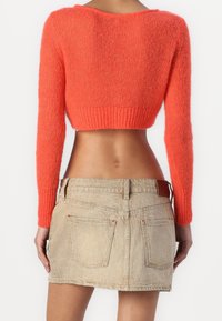 Krótki sweter dziergany w kolorze koralowym z długimi rękawami, zestawiony z jasnobeżową spódnicą jeansową z dwoma tylnymi kieszeniami i subtelnymi detalami przeszyć.