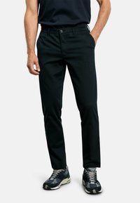 Pantaloni neri a taglio dritto con una consistenza liscia e una leggera lucentezza. Presentano una chiusura con bottone e tasche laterali. Indossati con sneakers a fantasia.