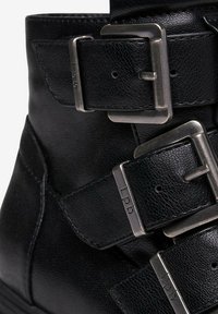 Bottine en cuir noir avec trois boucles en métal ajustables et finition texturée. Dotée de coutures renforcées et d'une semelle en caoutchouc basse.