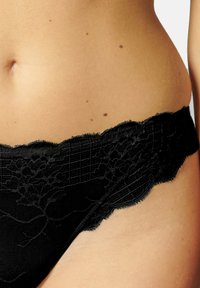 Gros plan de la taille féminine portant des sous-vêtements en dentelle noire avec un motif floral sur un fond de peau claire.