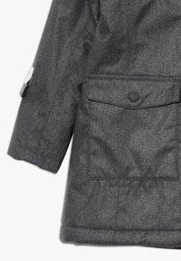 Šedý herringbonový blazer s knoflíkovým zapínáním, přední kapsou se klopou a reflexním akcentem na rukávu. Pevná textilie.