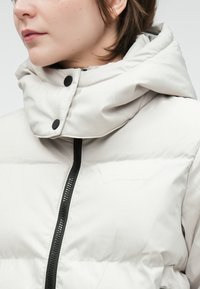 Jasnoszara kurtka typu puffer z wysokim kołnierzem, wyposażona w czarny zamek błyskawiczny i zatrzaski. Gładka faktura z dyskretnymi detalami szycia.