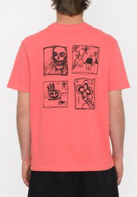 T-shirt corail à manches courtes avec des illustrations graphiques noires au dos, comprenant quatre motifs distincts : crâne, maison hantée, citrouille et fleur.