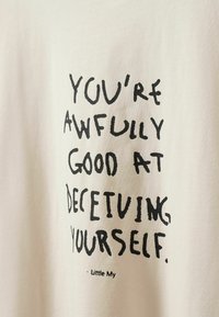 Κείμενο σε μπεζ ύφασμα λέει "You're awfully good at deceiving yourself.", υπογεγραμμένο από τη Μικρή Μάι με μαύρη χειρόγραφη γραμματοσειρά.