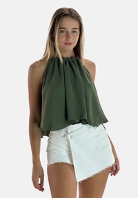 Top sin mangas verde oliva con escote fruncido, combinado con shorts de mezclilla blancos que presentan un diseño envolvente único y un dobladillo deshilachado.