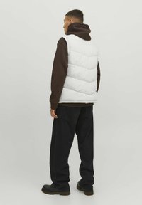 White puffer vest with diagonal quilted pattern over a brown hoodie, paired with black loose-fitting jeans and black boots.