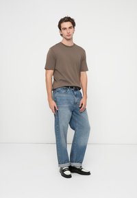 Rjava majica s kratkimi rokavi, svetlo modre široke kavbojke iz jeansa, črno-bele loaferje. Preprost dizajn, enobarvni, sproščen kroj in zavihani robovi kavbojk.