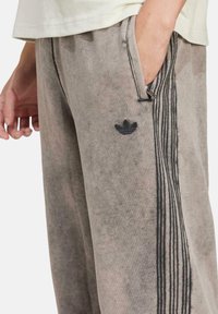 Grå sweatpants med en mjuk textur, med svarta tre-rands detaljer längs sidorna och en liten svart logotyp på låret.