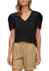 Zwarte V-hals top met pofferige mouwen en kantdetails op de schouders, gecombineerd met lichtbruine shorts met een trekkoord tailleband.