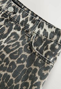 Jean en denim à imprimé léopard avec des tons gris et beige, des accessoires en argent, une poche avant et une finition légèrement texturée.