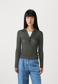 Dunkelgrünes, geripptes Langarm-Polohemd mit Kragen und einer Dreiknopf-Leiste, kombiniert mit hellblauen, locker sitzenden Jeans.