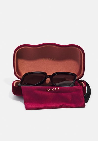 Gafas de sol negras en un estuche de terciopelo burdeos con el logo dorado "GUCCI", acompañadas de un pouch de limpieza a juego en burdeos.
