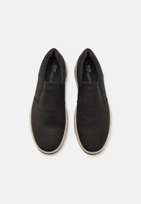 Chaussures noires à enfiler avec une tige en cuir lisse, bout arrondi et accents perforés. Semelle en caoutchouc de couleur claire avec une texture subtile.