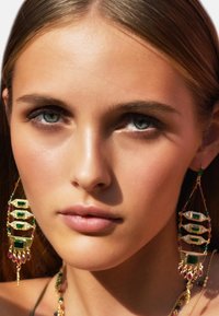 Boucles d'oreilles dorées ornées de pierres précieuses vertes et rouges, présentant un design en couches avec des formes géométriques et des accents décoratifs. Détails complexes présents.