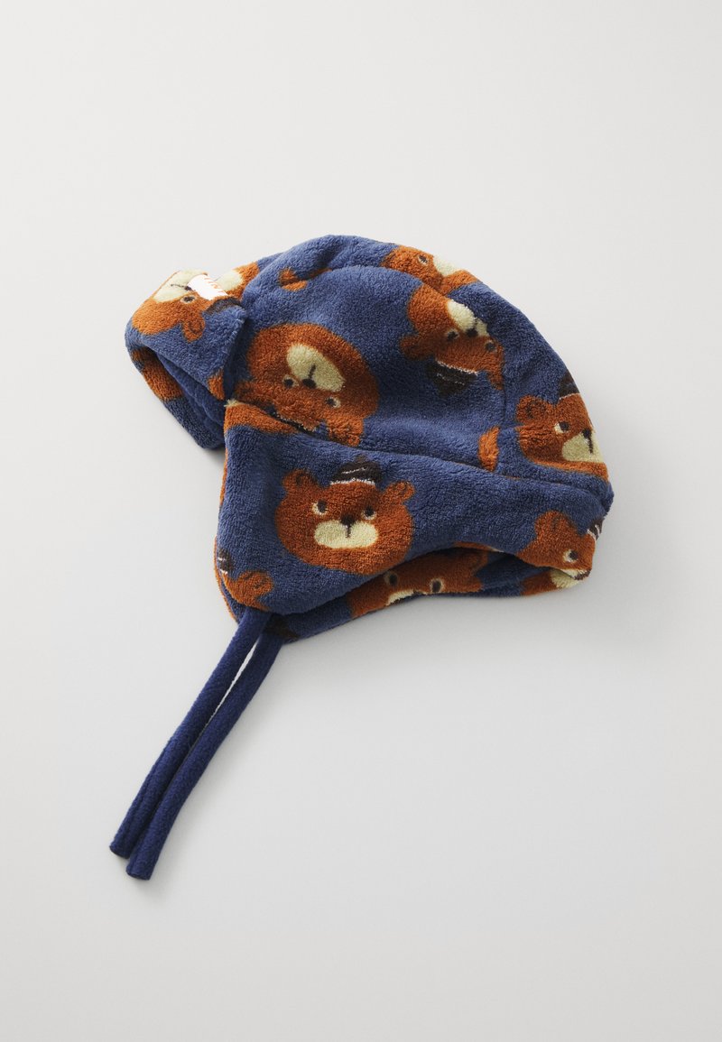 Fleece hat in dark blue with a playful bear pattern in brown and cream. Features ties for adjustment and a soft, textured finish.