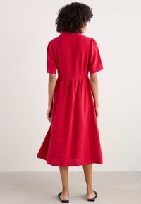 Rotes Leinenkleid mit kurzen Ärmeln, Kragen, tailliertem Schnitt und weiter Rockform. Minimalistisches Design mit glatter Textur und knöchellangem Saum.