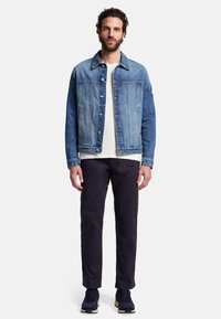 Jasnoniebieska kurtka dżinsowa z zapięciem na guziki, dwiema kieszeniami na piersi i lekko skróconym dołem. Połączona z ciemnymi spodniami i granatowymi sneakerami.