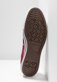 Rote Segeltuchsportschuhe mit oberer Sohle aus weißem Gummi, braunem strukturiertem Laufsohle, Metallösen und einem schwarzen Streifen entlang der Sohle. Logo auf der Sohle.