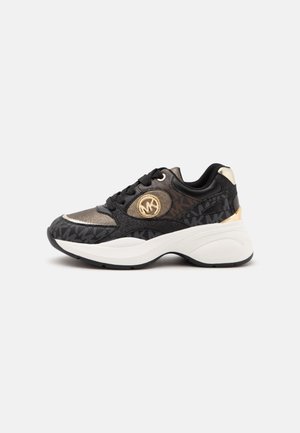 Sort og guldfarvet sneaker med tyk hvid sål, sidelæse, og cirkulært gyldent logo på ydersiden, vist på en ensfarvet lys baggrund.