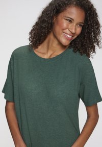 Zaļā ribotā T-krekla īsām piedurknēm, apaļu kakla izgriezumu un maigu faktūru. Piedāvā brīvu piegriezumu un minimālistisku dizainu.