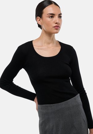Haut noir à manches longues en tissu côtelé, avec un décolleté rond et une coupe ajustée, associé à une jupe en chevrons grise.