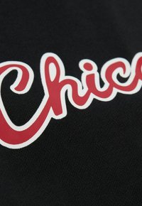 Tissu noir avec un gros plan du mot "Chic" en lettres rouges vives soulignées de blanc, présentant une texture lisse et un style de police décontracté.