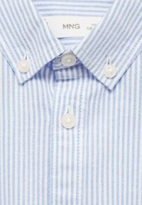 Chemise à rayures bleues claires et blanches avec un col pointu, dotée de deux boutons au col et d'une texture de tissu douce.