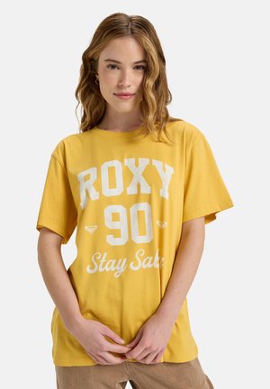 T-shirt en coton jaune avec le texte graphique blanc "ROXY 90 Stay Safe." Coupe décontractée, manches courtes, col rond. Texture lisse.