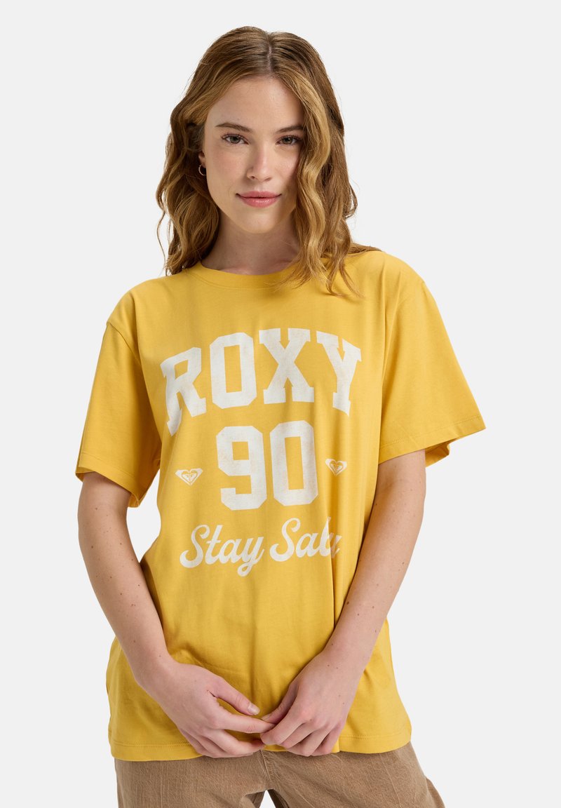 Geel katoenen t-shirt met witte grafische tekst "ROXY 90 Stay Safe." Losse pasvorm, korte mouwen, ronde halslijn. Gladde textuur.
